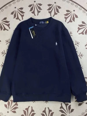 Mörkblå sweatshirt från Polo Ralph Lauren - Klassisk mörkblå sweatshirt från Polo Ralph Lauren med broderad logga på bröstet. Tröjan har rund halsringning, ribbade muddar och är långärmad. Perfekt för en clean och stilren look.