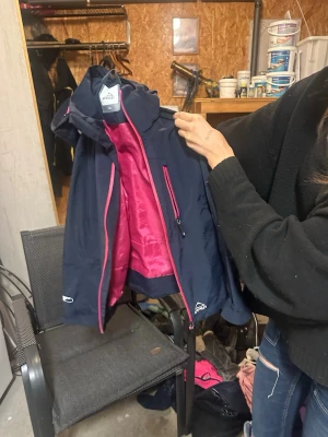 Mörkblå vindjacka från McKinley - Säljer en mörkblå vindjacka från McKinley med rosa detaljer och foder. Jackan har huva, dragkedja framtill och praktiska fickor med rosa dragkedjor. Perfekt för blåsiga dagar och outdoor-äventyr.