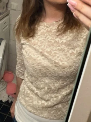 Beige spetsblus från Brittany Black - Säljer en beige blus från Brittany Black med blommigt spetsmönster. Det står L på toppen men den är liten i storleken:) Blusen har rund halsringning och trekvartsärm. Materialet är genombrutet och ger en snygg, feminin vibe. Perfekt för dig som gillar detaljer och vill sticka ut lite extra.