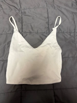 Ljusbeige croppad väst från Amisu - Säljer en stilren ljusbeige croppad linne från Amisu i storlek XS. Linnet har tunna axelband och v-ringad halsringning, Materialet är mjukt och följsamt syntet.