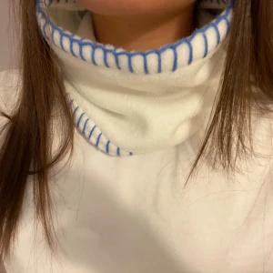 Vit buff med blåa stygn  - Handsydd buff med blåa stygn i vit färg!