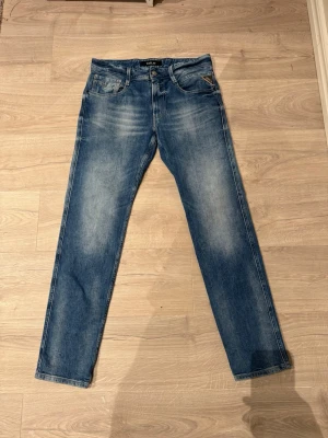 Replay Anbass - Snygga Replay Anbass jeans i klassisk blå tvätt med lätt slitning och raka ben. Jeansen har fem fickor, gylf med dragkedja och Replay-logga på bakfickan samt läderpatch i midjan. Perfekta för dig som gillar en stilren och tidlös look.