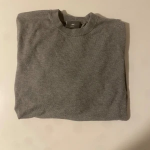 Grå slim fit tröja från H&M - En stilren grå tröja från H&M i slim fit-modell. Tröjan har rund halsringning, långa ärmar och ribbade muddar vid ärmslut och nederkant. Perfekt basplagg för lager på lager och enkel att matcha med allt.