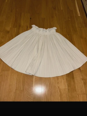 Vit plisserad kjol från Ginatricot - Supersöt vit kjol från Ginatricot i storlek 34. Kjolen är kort, har plisserade veck och en bred resår i midjan med volangkant upptill. Perfekt för dig som vill ha en fräsch och luftig look till sommaren.