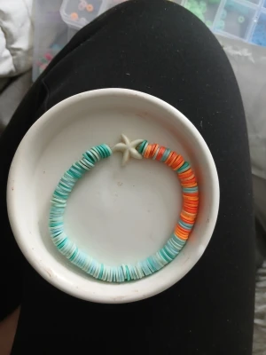 Färgglad pärlarmband med sjöstjärna - Handgjort armband med platta pärlor i turkos, mintgrön, orange och ljusblå samt en vit sjöstjärna i mitten. Stretchigt och bekvämt, perfekt för att ge en somrig vibe till din outfit.