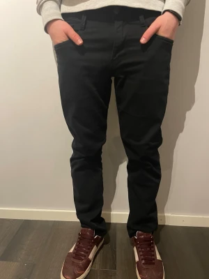 Svarta Replay Anbass jeans 30/32 - Säljer ett par svarta Replay Anbass jeans i storlek 30/32. De har en slim passform med klassisk femficksdesign och bälteshällor. Jeansen är tillverkade i ett mjukt bomullsmaterial med lite stretch för extra komfort. Snygga och stilrena svarta jeans som passar till det mesta.