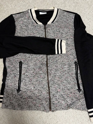 Svart och vit kofta från Vila - Säljer en snygg kofta från Vila med svart rygg och ärmar, samt vitmelerad framsida med små färgdetaljer. Tröjan har dragkedja, ribbade muddar och krage i svartvitt. Två fickor framtill (obs enbart för design, se bild) med coola detaljer. Perfekt för dig som gillar sportig stil.