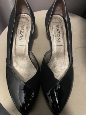 Svarta pumps från Mazzini Stockholm - Snygga pumps skor från Mazzini Stockholm i svart med spetsig tå. Skorna har en mix av blankt och matt material, vilket ger en cool kontrast. De är gjorda i Spanien i läder av hög kvalitet. Perfekta för dig som vill ha en stilren och trendig look. Storlek 38. Säljs i befintligt skick men är i väldigt bra skick! Hör av dig vid intresse🤗