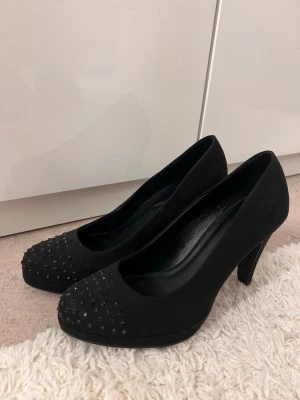 Svarta pumps med nitar från Graceland - Säljer ett par svarta pumps från Graceland i mockaimitation med rund tå och hög klack. Skorna har små svarta nitar framtill som ger en extra edge. 