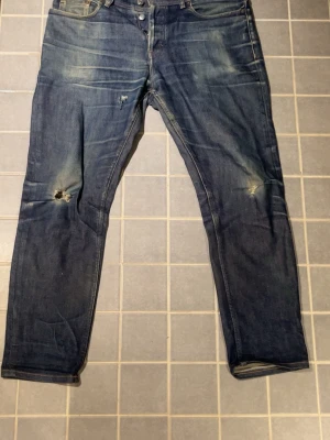 Selvage acne studio jeans 31/32 - Säljer ett par blå jeans från Blå Konst, tillverkade i Italien. Klassisk femficksmodell med raka ben och slitningar på knäna för en cool, använd look. Jeansen har knappgylf och tydliga kontrastsömmar.
