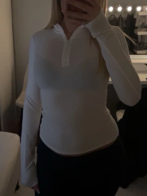 Vit långärmad träningstopp med half zip - Säljer en vit långärmad träningstopp med half zip framtill. Toppen är tight i passformen.