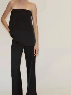 Svart axelbandslös tubtopp i satin - Säljer en svart axelbandslös tubtopp i glansigt satinmaterial. Toppen har en bandeauformad siluett och faller snyggt över kroppen för en clean och stilren look. Perfekt att styla med vida byxor eller kjol. Helt oanvänd med lapp kvar. 