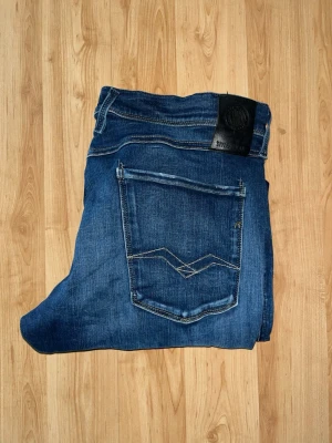 Replay Hyperflex Anbass jeans  - Säljer dessa snygga Replay Hyperflex Anbass jeans i mörkblå tvätt med snygga slitningar. Midja 45cm, längd 104cm. JAG SKICKAR EJ FLER BILDER NÄR JAG BÄR JEANSEN! för bättre inblick i passformen rekommenderar jag att googla på modellnamnet. För storleksguide kolla måtten noggrant då jeansen alltid kan vara uppsydda heller krympta och jag ej tar emot returer :) 1,17