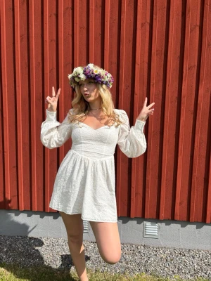 Vit kort klänning med puffärmar - Superfin vit kort klänning med broderade detaljer och långa puffärmar. Klänningen har v-ringning och markerad midja som ger en smickrande siluett, knyten i ryggen! Perfekt för student eller examen!