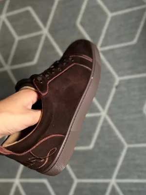 Bruna mockasneakers från Louboutin - Säljer ett par bruna sneakers från Christian Louboutin i mjuk mocka med signaturröd sula och diskreta broderidetaljer. Skorna har snörning, beige innerfoder och klassisk rund tå. Perfekta för dig som vill ha något lyxigt och stilrent.