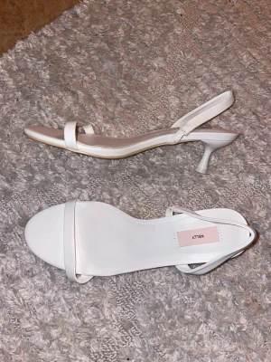 Vita sandaler med låg klack från Nelly - Säljer ett par stilrena vita sandaler från Nelly med smal rem över tårna och runt hälen. Skorna har låg klack och öppen tå, perfekta till sommarens outfits.