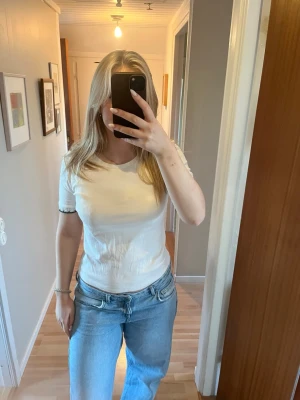 Vit t-shirt med virkade detaljer - Vit t-shirt i bomull med korta ärmar och rund hals. Ärmsluten har virkade detaljer i vitt och svart som ger en unik touch. Passformen är normal och materialet känns mjukt och skönt mot huden. Perfekt till jeans eller kjol för en chill look.