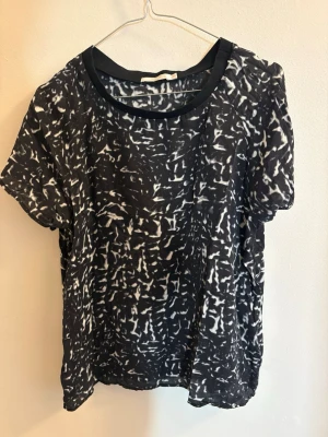 Svartvit mönstrad blus Wera - Säljer en luftig svartvit blus från Wera med abstrakt mönster. Blusen har rund halsringning med svart kant och korta ärmar. Materialet känns lätt och flowy, perfekt till jeans eller kjol för en chill look.