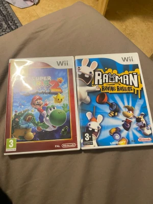 Super Mario Galaxy 2 & Rayman Raving Rabbids (Wii) - Två populära Wii-spel: Super Mario Galaxy 2 och Rayman Raving Rabbids. Båda fodralen ser ut att vara i fint skick utan synliga skador. Perfekt för dig som vill utöka din samling eller återuppleva klassiska spel på Nintendo Wii.