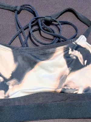 Mönstrad sportväst med snörning - Säljer en sportig väst med unikt mönster i svart, beige och grå toner. Västen har tunna axelband som korsas i ryggen och ger en snygg snörningsdetalj. Materialet är stretchigt och passar perfekt till träning eller yoga.