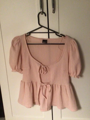 Ljusrosa blus med knyt från Gina Tricot - Söt rosa blus med rosetter och volanger. Använd 2-3 gånger, bra skick. Storlek xs