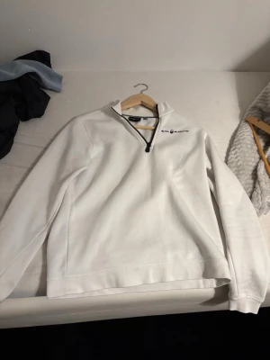 Vit Sail Racing half zip sweatshirt - Säljer en clean vit sweatshirt från Sail Racing med svart logga på bröstet och half zip-dragkedja. Insidan är mjuk och fleecefodrad för extra komfort. Perfekt till chill dagar eller när du vill ha en enkel men snygg look.