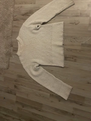 Vit stickad tröja med bred mudd - Mysig vit stickad tröja med bred ribbad mudd nertill och vid ärmsluten. Tröjan har en klassisk rund halsringning och långärmade ärmar. Perfekt för kyliga dagar och enkel att matcha med jeans!