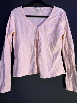 Ljusrosa kofta från H&M, M - Säljer en ljusrosa kofta från H&M i storlek M. Koftan har v-ringad hals, långa ärmar och knappar framtill. Materialet är mjuk bomull med ett diskret prickigt mönster. Perfekt att slänga på sig när det är lite kyligt ute.