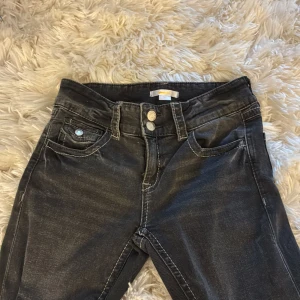 Svarta jeans från Gina Tricot, stl 164 - Snygga svarta jeans från Gina Tricot med dubbla silverknappar i midjan och klassiska fem fickor. Jeansen har tydliga vita sömmar och en något tvättad look. Perfekta för dig som gillar en stilren och enkel vibe. 