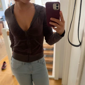 Brun velour hoodie med dragkedja - Mysig brun hoodie i velour med dragkedja framtill och huva. Tröjan har långa ärmar, ribbade muddar och en djup v-ringning. Perfekt för chill dagar eller när du vill ha en avslappnad look.