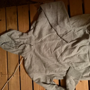 Grå hoodie från McKenzie i bomull - Säljer en stilren grå hoodie från McKenzie i mjuk bomull. Tröjan har huva med dragsko, magficka och långa ärmar med ribbade muddar. Perfekt för chill dagar eller när du vill ha en enkel och clean look.