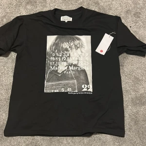 Maison Margiela svart t-shirt med print - Svart t-shirt från Maison Margiela med stort grafiskt print framtill i gråskala och klassisk logga. T-shirten har rund hals. Denna t shirten är oversized för dig som gillar det tveka ej att skriva 
