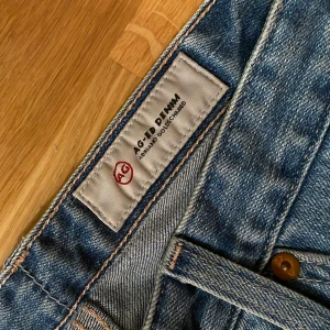 AG Jeans croppade  - Snygga ljusblå jeans från AG Adriano Goldschmied med croppad längd och råa, slitna kanter. Modellen har raka ben, hög midja och slitningar vid knäna för en cool vibe. Klassisk femficksdesign och tillverkade i mjukt denimtyg.