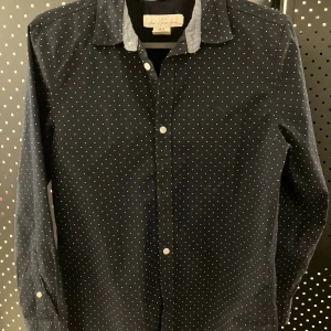 Mörkblå prickig skjorta från L.O.G.G. H&M - Snygg mörkblå skjorta från med vita små prickar över hela tyget. Klassisk krage, långa ärmar och knäppning framtill. Skjortan är i mjuk bomull och har en stilren look som passar perfekt till jeans eller chinos. Använts 1 gång! 