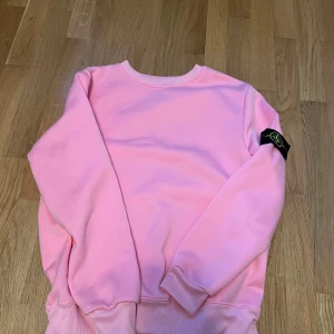 Rosa Stone Island sweatshirt - Säljer en rosa sweatshirt från Stone Island med klassisk logga på ärmen. Tröjan har rund halsringning, ribbade muddar och är tillverkad i mjuk bomull. Perfekt för dig som vill sticka ut med en färgglad och stilren look. Den passar mest S men M funkar oxå pris kan diskuteras fraktar samma dag! 