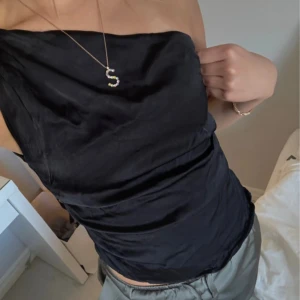 Svart oneshoulder topp från Zara - Säljer en svart, glansig oneshoulder topp från Zara i storlek S. Toppen har en elegant asymmetrisk axel och är figurnära med en lätt draperad effekt. Perfekt för dig som gillar stilrena och trendiga plagg.