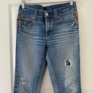 Blå bootcut jeans från Giordano Blues - Bootcut jeans i mellanblå tvätt från Giordano Blues, med slitna detaljer och hål på benen för en cool, avslappnad look. Klassisk femficksmodell i 100% bomull. Perfekta för dig som gillar en lite mer edgy stil.