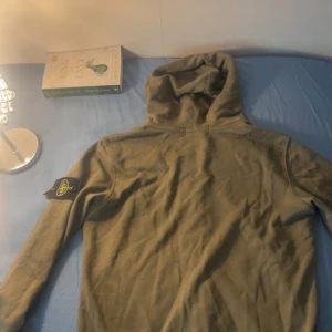 Beige hoodie från Stone Island - Säljer en beige hoodie från Stone Island med klassisk logotyp-patch på vänster ärm. Tröjan har huva och långa ärmar, perfekt för chill dagar. Materialet är mjukt och känns skönt mot huden. Snygg och enkel design som funkar till många olika stilar.