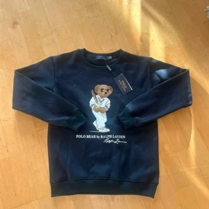 Mörkblåa Ralph Lauren Polo Björn Tröja - Mörkblå sweatshirt från Ralph Lauren med ikoniska Polo Bear-trycket framtill. Tröjan är i mjuk bomullsmix. Helt ny, aldrig andvänts. 