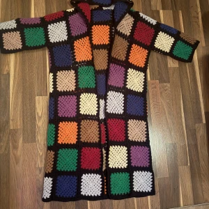 Färgglad lång cardigan jacka - Unik lång cardigan jacka med virkade rutor i flera färger som lila, grön, blå, orange, röd och beige. Jackan har lång ärm och öppen framtill, perfekt för dig som gillar retro och stickat. Rutigt mönster och mjukt stickat material.