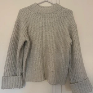 Vit stickad tröja med grov struktur - Säljer en vit stickad tröja med grov ribbad struktur och högre rund hals. Tröjan har långa ärmar och breda muddar vid ärmslut och nederkant. Perfekt för en höststil.