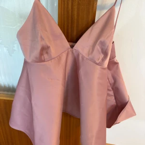 Rosa linnetopp från H&M - Säljer en ljusrosa linnetopp från H&M med smala axelband och v-ringad front. Toppen har en lätt utsvängd passform och är tillverkad i ett slätt, satinliknande material som ger en lyxig känsla. Perfekt för varma dagar eller när du vill känna dig extra fin.