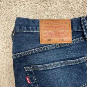 Levi's 501 blå jeans W33 L32 - Klassiska Levi's 501 jeans i mörkblå denim med raka ben och normal passform. Byxorna har fem fickor, knappgylf och den ikoniska läderpatchen bak i midjan. Perfekta för en avslappnad och tidlös look.