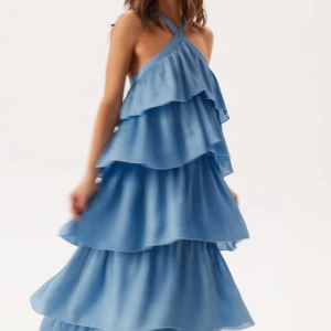 Blå volangklänning med korsade band - Superfin långklänning i ljusblått med flera lager volanger och korsade axelband i ryggen. Perfekt balklänning, bröllopsgäst-klänning eller bara när du vill klä dig i en superfin klänning! Klänningen är oanvänd. 