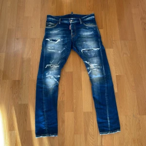 Dsquared2 blå slitna jeans, stl 46 - Säljer ett par blå jeans från Dsquared2 i modellen Sexy Twist Jean. Jeansen har en snygg slitning och flera revor framtill för en cool, trendig look. Klassisk femficksmodell med normal passform och raka ben. Materialet är jeans i bomull.