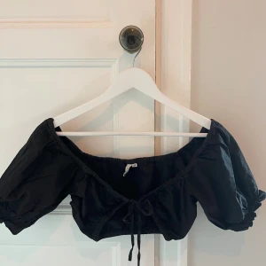 Svart croptop från NLY Trend, strl 34 - Svart topp från Nelly i storlek 34 med knyt fram i kort modell.