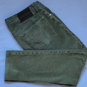 Gröna Jacob Cohën byxor - Snygga gröna bomullsbyxor från Jacob Cohën med klassisk femficksdesign, läderpatch bak och diskreta broderade detaljer. Byxorna har normal passform och är tillverkade i mjuk tyg som ger en avslappnad men stilren look. W34 men anser själv att den är mer W33. Självklart äkta, för mer info fråga! .