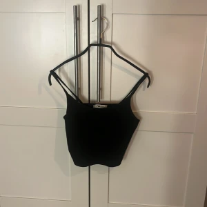 Svart croppad linnetopp från Sister - Säljer en svart croppad linnetopp från Sister i storlek S. Toppen har smala axelband och är tillverkad i ett stretchigt material som sitter snyggt på kroppen. Perfekt att matcha med jeans eller kjol för en cool look.