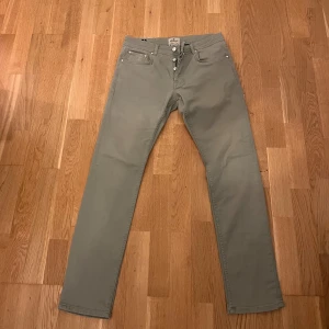 Olivgröna byxor från Morris, 33/32 - Snygga olivgröna byxor från Morris i modellen Atelier M. Byxorna har raka ben, klassisk femficksdesign och coola detaljer med logoknappar. Tillverkade i mjuk bomull för en skön känsla och stilren look.säljs vid billigt pris pga av unika färgen