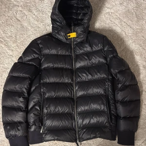 Parajumpers Sheen  - Säljer en svart Parajumpers Sheen dunjacka i storlek M. Jackan har en glansig finish, huva, dragkedja framtill och ribbade muddar. Insidan är grå med meshficka och coola detaljer. Perfekt för kalla dagar när du vill hålla stilen. Jackan är även i suveränt skick💫 (Köpt för 6990kr)